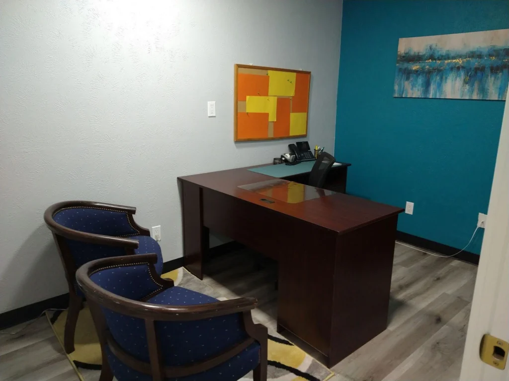 Private office, Suite B, with L-shaped office desk, ergonomic desk chair, two guest chairs, cork board, and private conference phone on desk