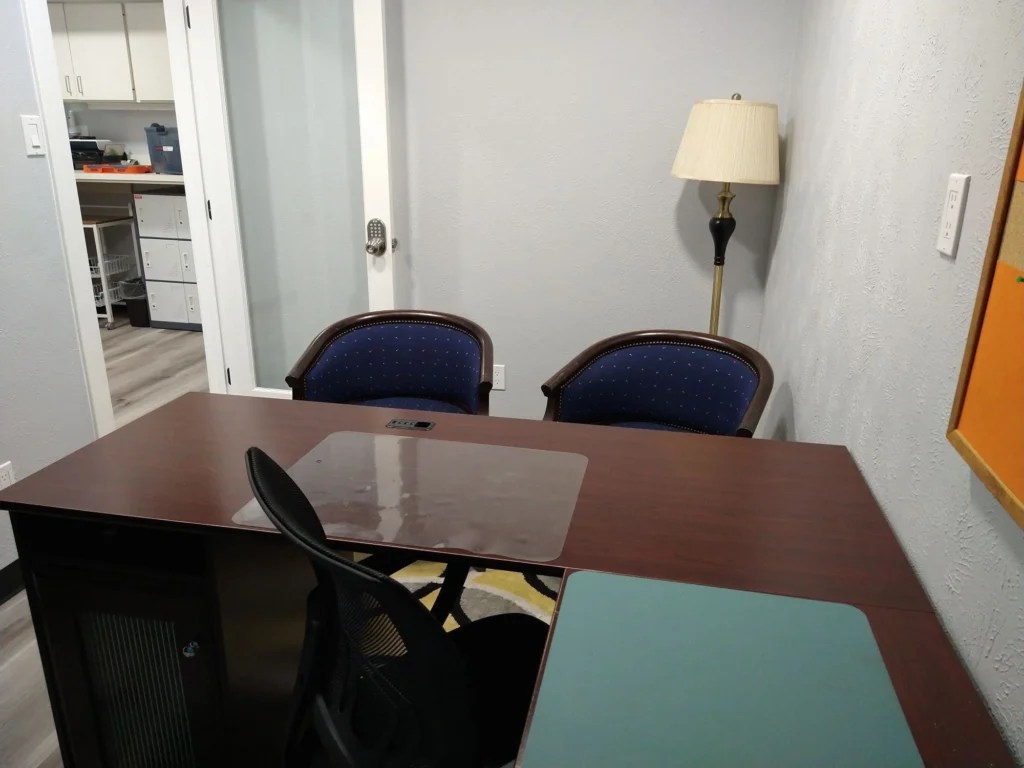 Private office, Suite B, with floor lamp, two guest chairs, and ergonomic desk chair at L-shaped executive desk