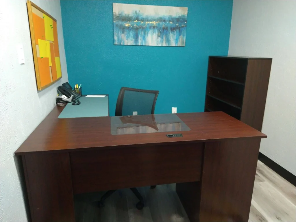 Private office, Suite B, with L-shaped executive desk, ergonomic desk chair, bookshelf, corkboard, and modern art