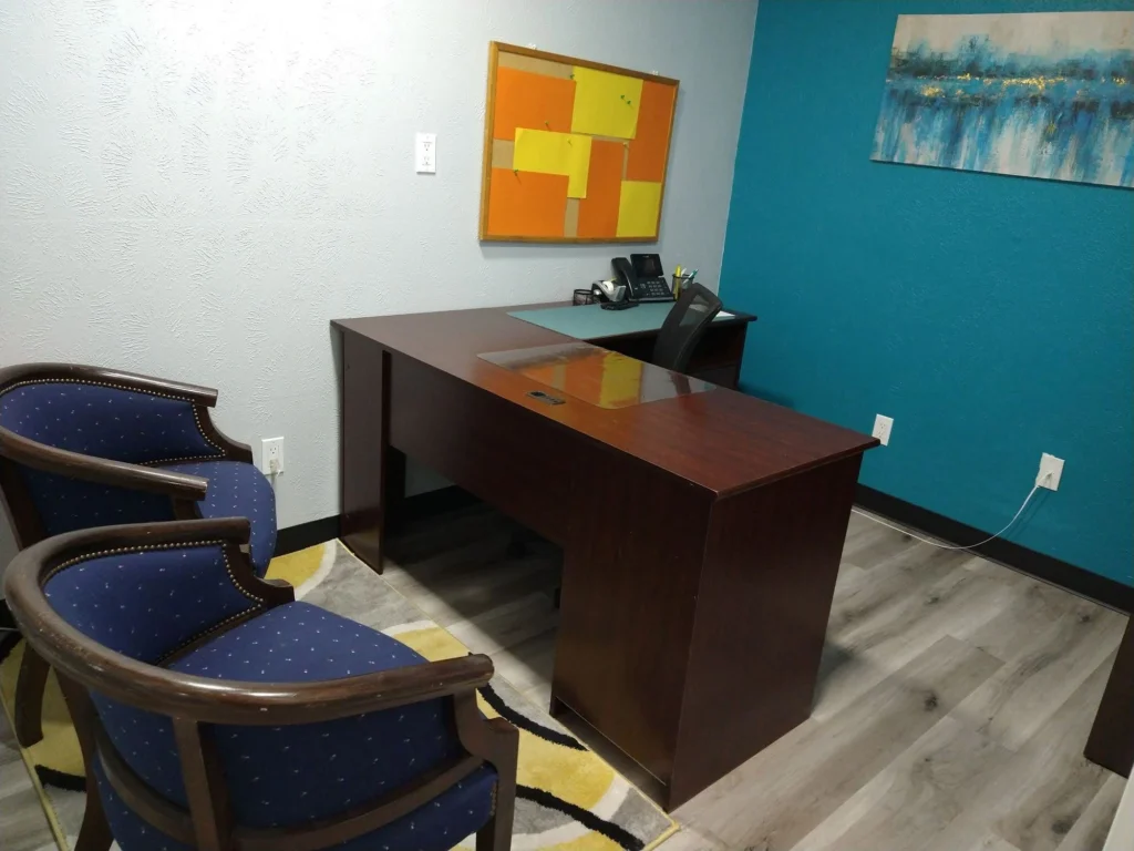 Private office, Suite B, with L-shaped office desk, ergonomic desk chair, two guest chairs, cork board, and private conference phone on desk