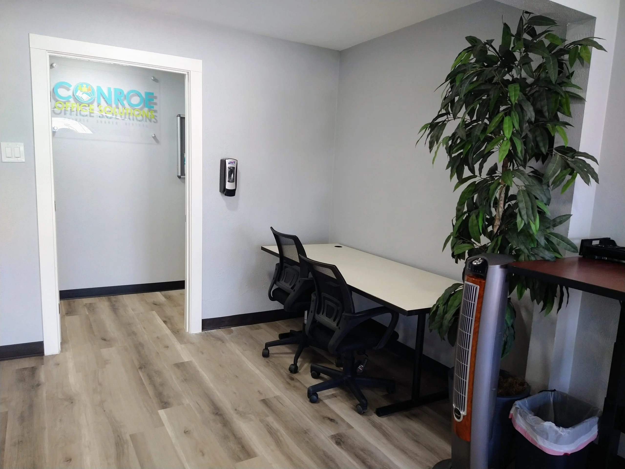 Coworking space in front lobby area with long table and two chairs and hand sanitizer dispenser on wall near door leading to private offices