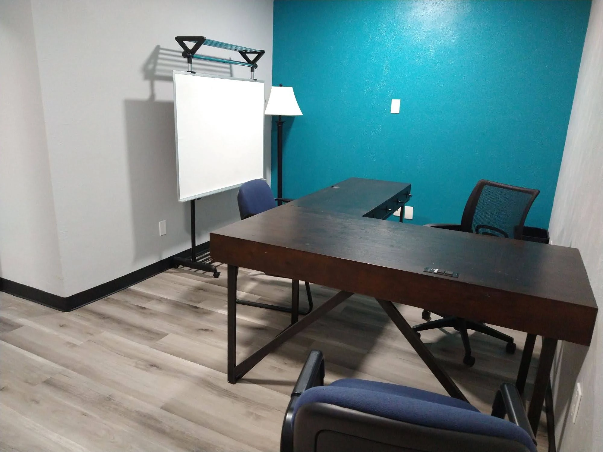 Private office Suite C, with mobile whiteboard, floor lamp, L-shaped desk, ergonomic desk chair, and two guest chairs